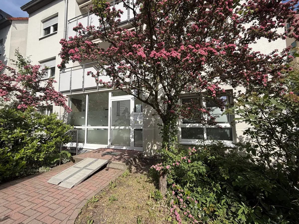 Eingang der Praxis in der Kleberstraße 26 mit blühendem Baum und Rampe