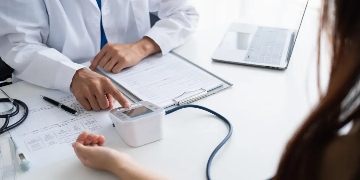 Arzt misst einer Patientin am Schreibtisch den Blutdruck